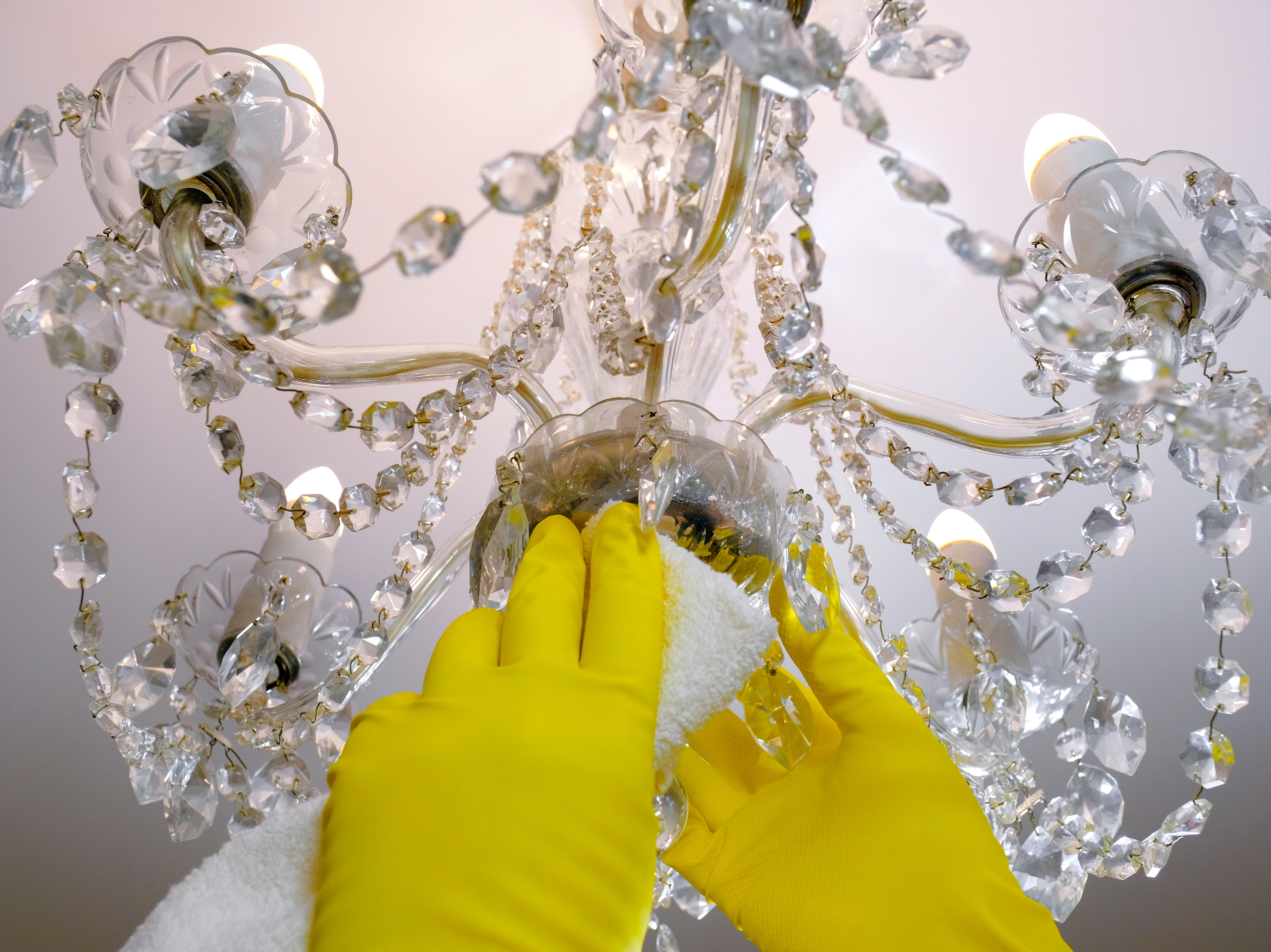 Close-up of gloved hands wipes dust from the chandelier. House cleaning.